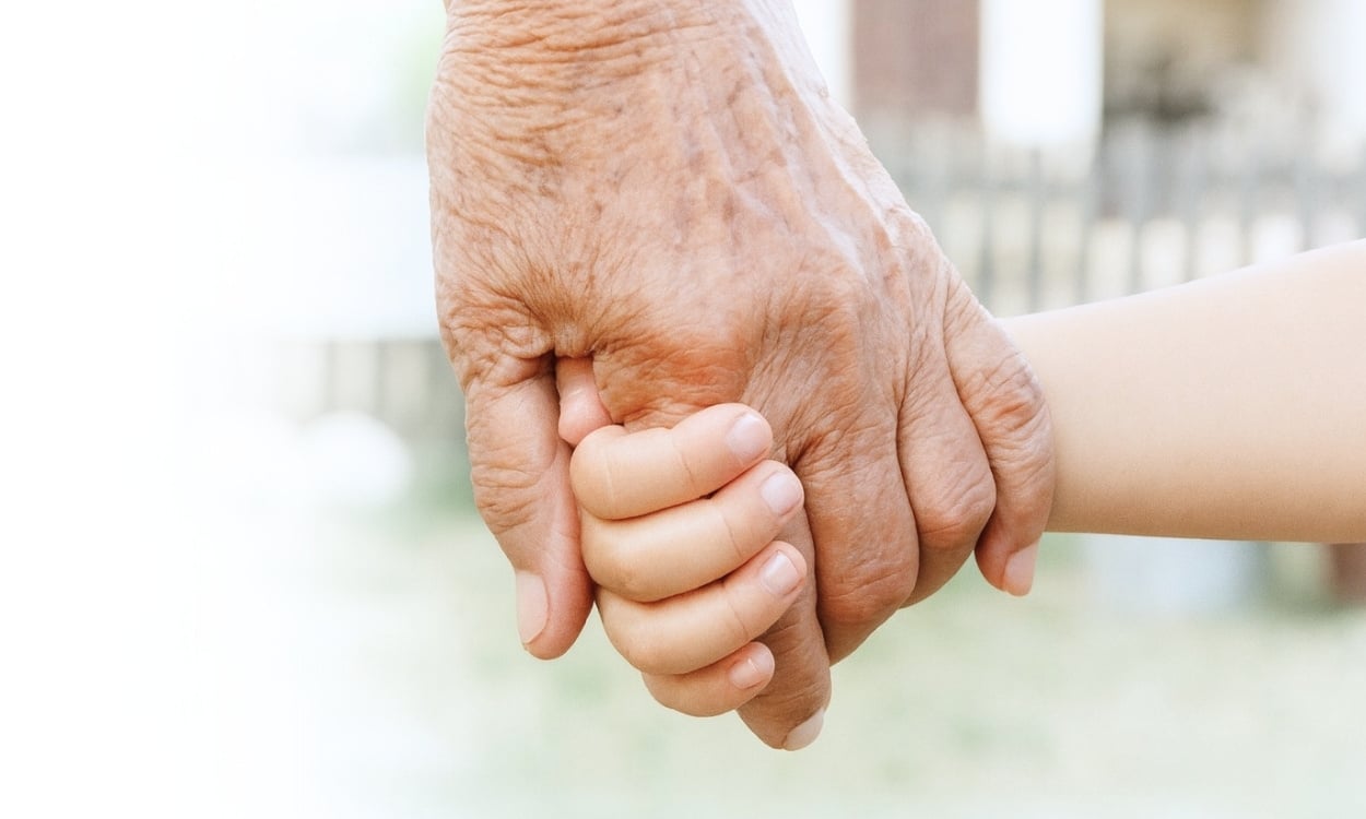 A close-up of a grandparent and child holding hands outdoors, reflecting trust and lifelong skin health and care.